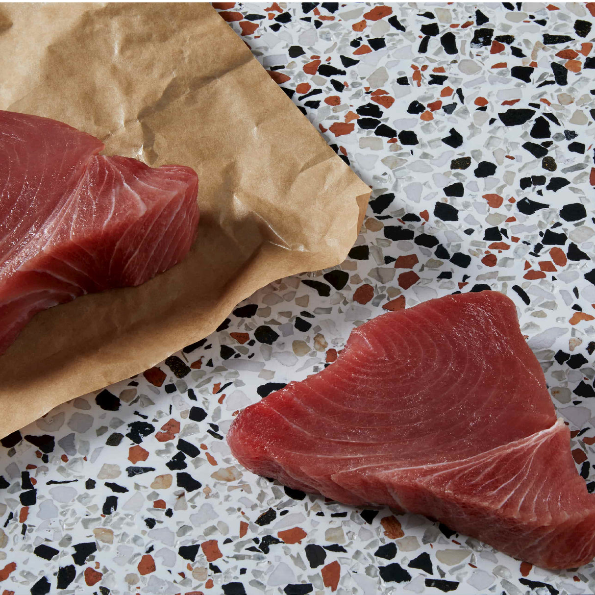 Cat Person Tuna Shreds in Broth, made with quality ingredients, are displayed on a terrazzo countertop—one portion on parchment, one on the surface—highlighting this protein-rich meal for your cat.