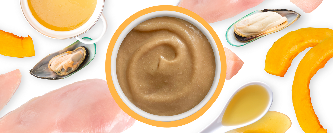 A bowl of creamy brown puree is surrounded by raw chicken slices, green-lipped mussels, pumpkin slices, and spoons of yellow liquid on a white background.