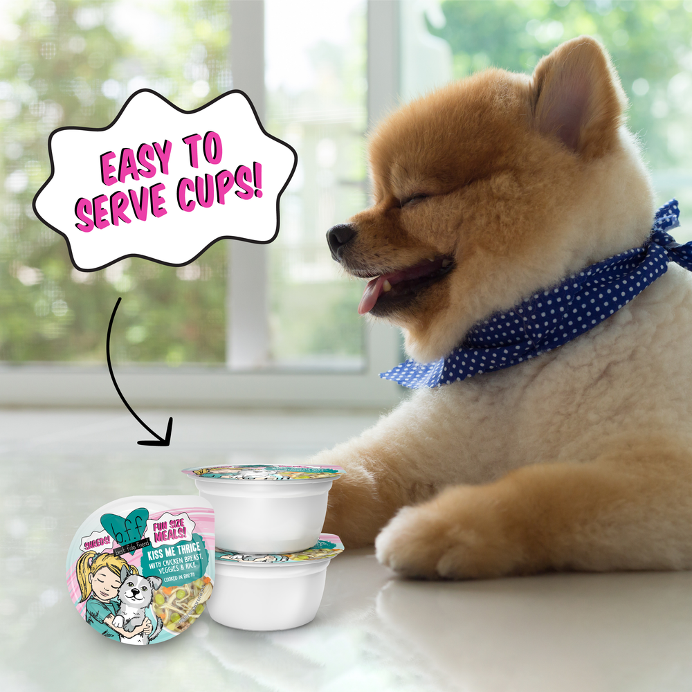 A fluffy brown Pomeranian in a blue polka dot scarf sits by two Kiss Me Thrice dog food cups from BFF Best Fido Friend, each with cartoon labels. A speech bubble says, “EASY TO SERVE CUPS!” Bright lighting shows the wholesome veggies inside.