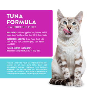 A light brown tabby cat with blue eyes sits and licks its lips beside a Weruva Wx Lickable Tuna Formula Cat Treat product label, which displays ingredients, nutritional details, and feeding guidelines for this low phosphorus hydrating purée.