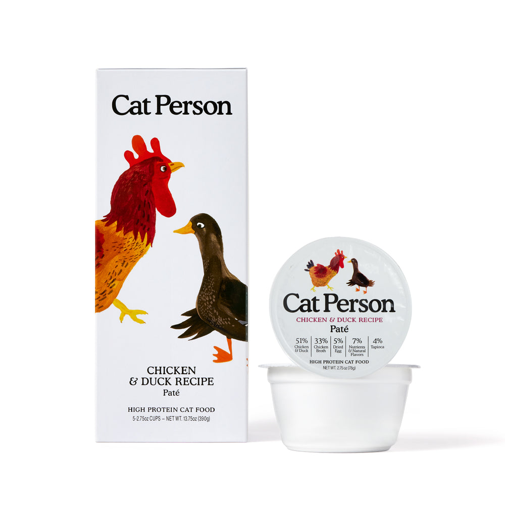 A package of Cat Person Chicken & Duck Paté cat food features illustrations of a chicken and a duck on the packaging, emphasizing balanced nutrition for cats.