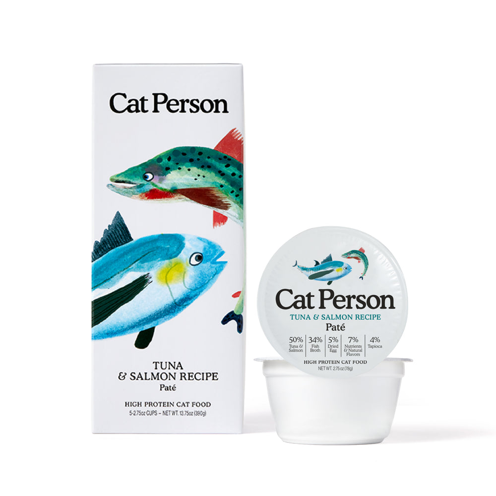 A box and container of Cat Person Tuna & Salmon Paté cat food, with colorful fish designs. The packaging emphasizes balanced nutrition for cats and displays product and nutritional details.