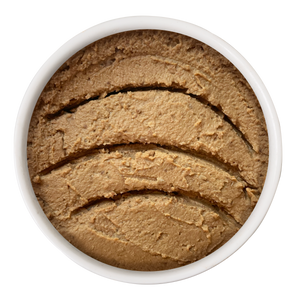 A white bowl holds Cat Person Tuna & Salmon Paté, a smooth, light brown blend for cats with several curved, evenly spaced grooves on its surface.