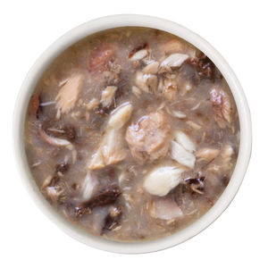 A white bowl filled with Weruva Salmon and Tuna Dinner in Gravy—chunky brownish soup with wild-caught salmon and meat—shown from above on a plain white background, a gourmet meal for discerning cats.