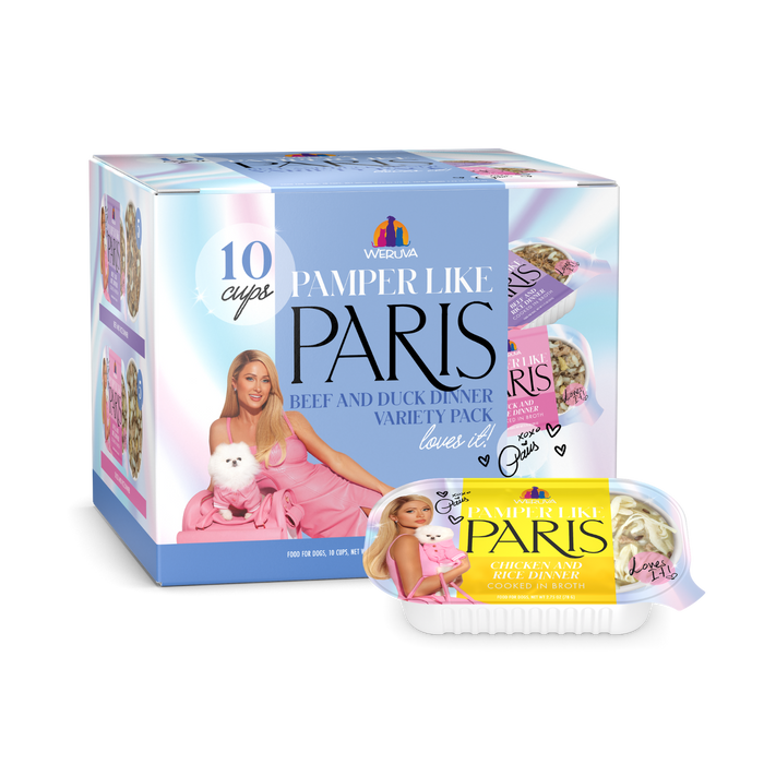 A blue box labeled Pamper Like Paris features Paris Hilton in a pink dress holding a small white dog. The box and food cup show images of her, with text advertising a beef, duck, and chicken dog food variety pack.